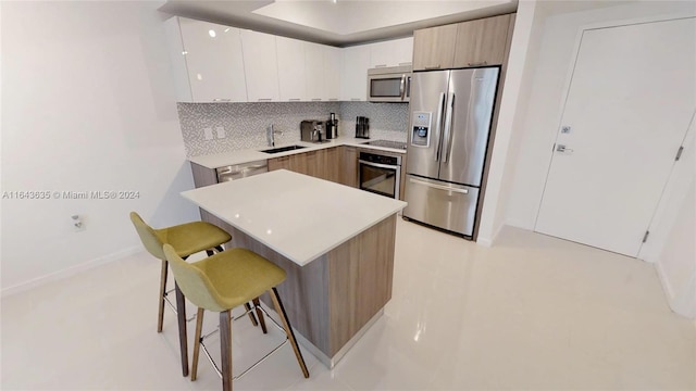 kitchen with stainless steel appliances, white cabinetry, sink, decorative backsplash, and a breakfast bar