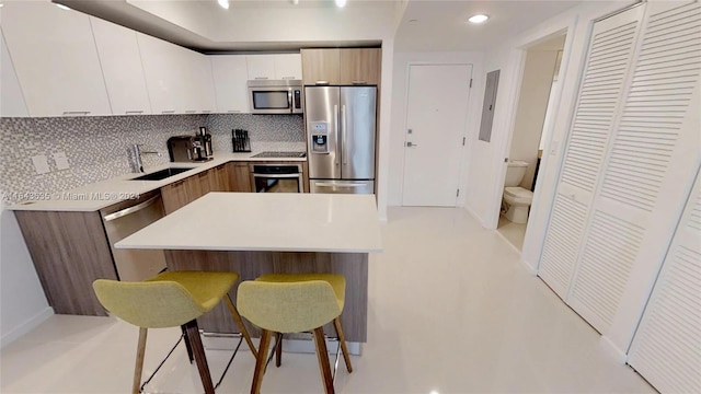 kitchen featuring white cabinetry, tasteful backsplash, sink, a breakfast bar, and appliances with stainless steel finishes