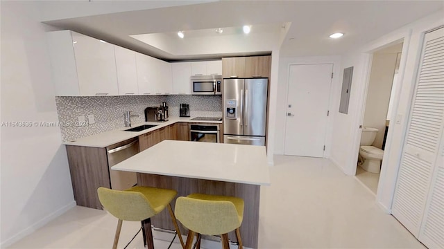 kitchen featuring white cabinets, stainless steel appliances, sink, kitchen peninsula, and a breakfast bar