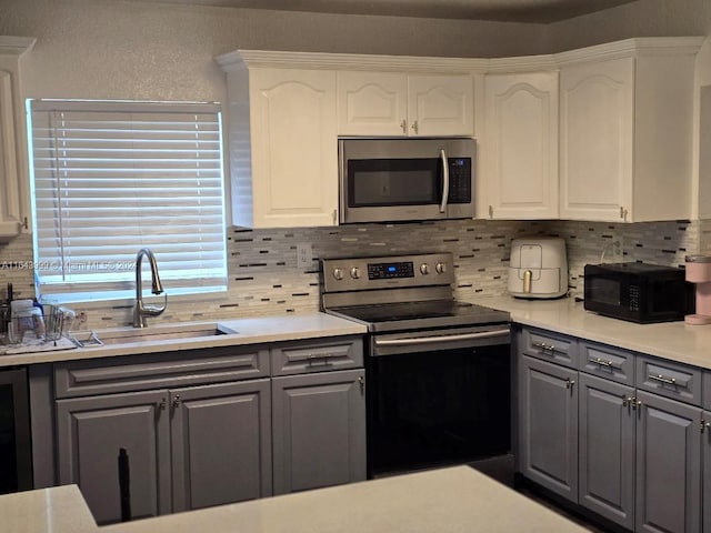 kitchen with backsplash, gray cabinets, white cabinetry, sink, and stainless steel appliances