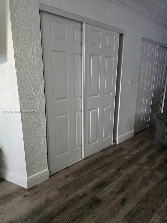 unfurnished bedroom with a textured wall, crown molding, dark wood-type flooring, and baseboards