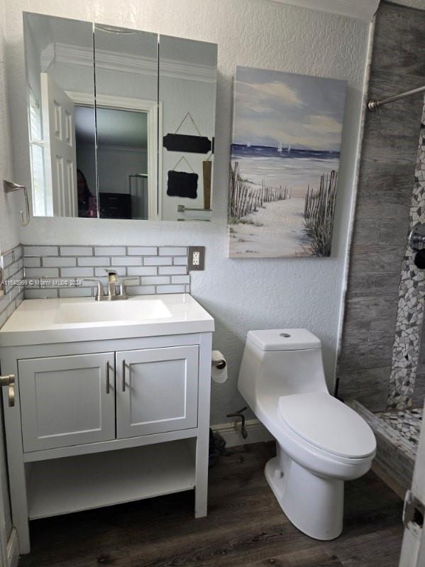 bathroom featuring tiled shower, wood-type flooring, decorative backsplash, vanity, and toilet