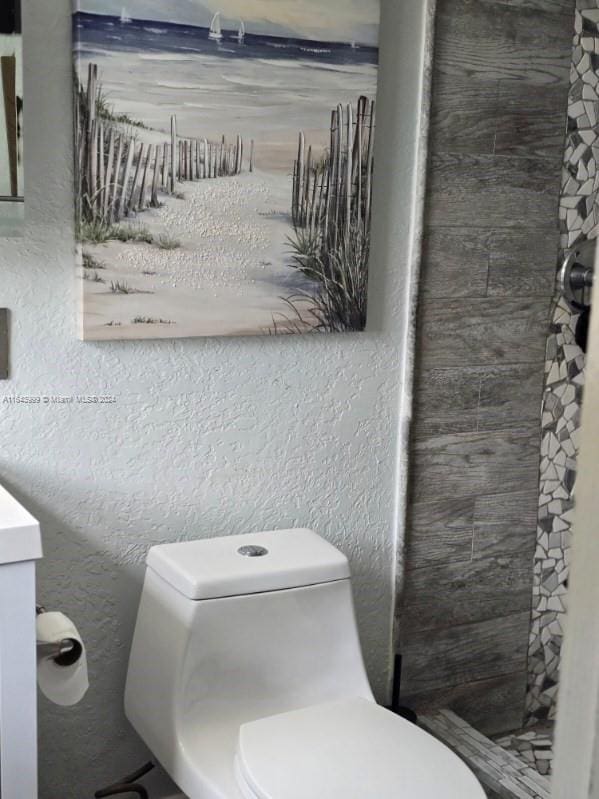 bathroom with toilet, a tile shower, and vanity