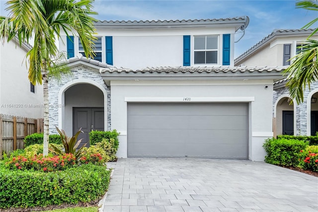 mediterranean / spanish-style home featuring fence, stucco siding, an attached garage, and decorative driveway