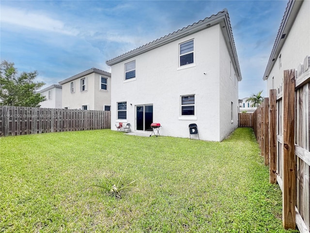 rear view of house featuring stucco siding, a lawn, and a fenced backyard