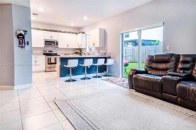 kitchen featuring open floor plan, a breakfast bar area, white cabinetry, stainless steel appliances, and a peninsula