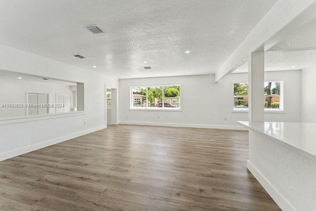 unfurnished living room featuring beam ceiling, a textured ceiling, and dark hardwood / wood-style floors