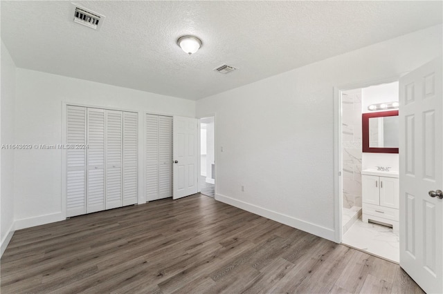 unfurnished bedroom featuring connected bathroom, dark wood-type flooring, a textured ceiling, and sink