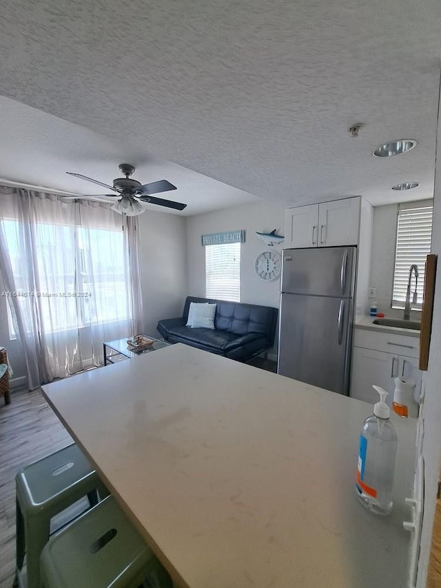 kitchen with ceiling fan, stainless steel refrigerator, white cabinetry, sink, and a textured ceiling