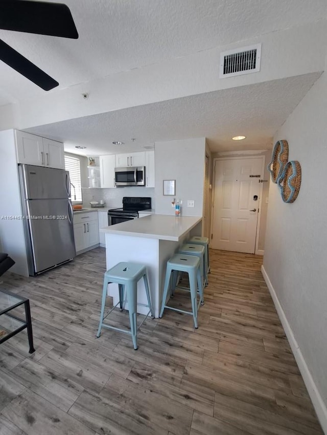 kitchen featuring stainless steel appliances, light hardwood / wood-style floors, white cabinetry, kitchen peninsula, and a breakfast bar