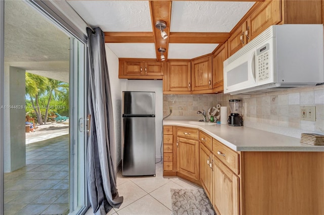 kitchen featuring beam ceiling, tasteful backsplash, sink, stainless steel refrigerator, and light tile patterned flooring