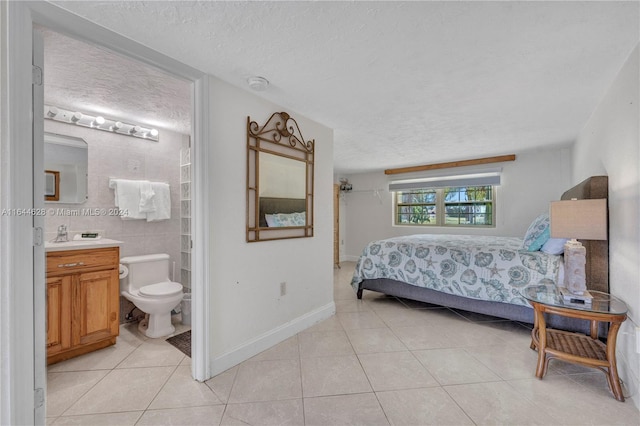 bedroom with a textured ceiling, ensuite bathroom, and light tile patterned floors