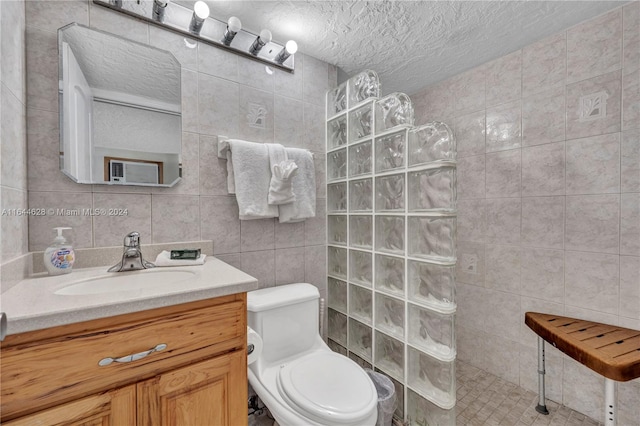 bathroom with a tile shower, a textured ceiling, vanity, tile walls, and toilet