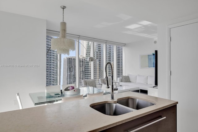 kitchen featuring a city view, a sink, dark brown cabinetry, a wall of windows, and hanging light fixtures