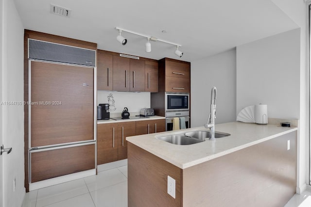 kitchen featuring light tile patterned floors, visible vents, a peninsula, a sink, and built in appliances