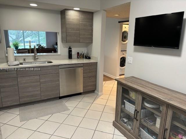 kitchen featuring stacked washer / drying machine, light tile patterned flooring, sink, dark brown cabinets, and stainless steel dishwasher