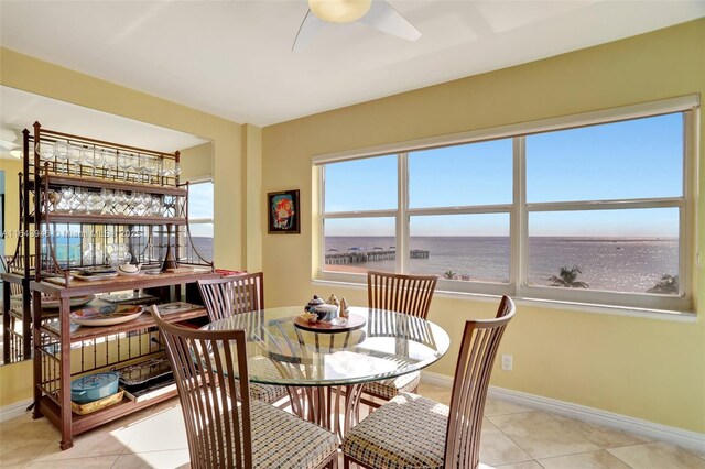 tiled dining space with ceiling fan and a water view