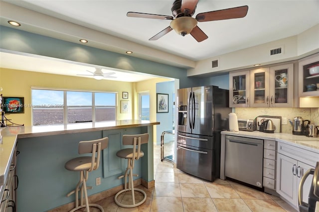 kitchen featuring light tile patterned floors, backsplash, appliances with stainless steel finishes, ceiling fan, and a water view