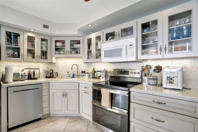 kitchen with stainless steel appliances, light stone countertops, light tile patterned floors, decorative backsplash, and sink