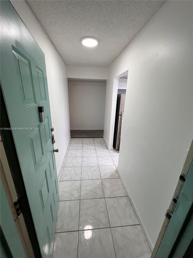 hallway with a textured ceiling and light tile patterned floors