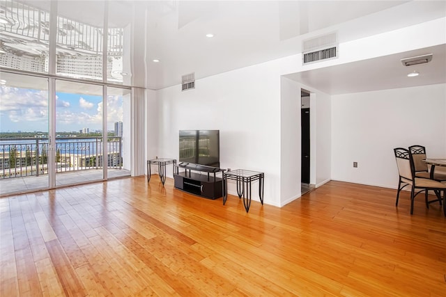 living room with a towering ceiling, light hardwood / wood-style floors, and floor to ceiling windows