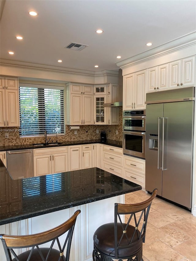 kitchen featuring a breakfast bar area, light tile patterned floors, tasteful backsplash, stainless steel appliances, and dark stone countertops