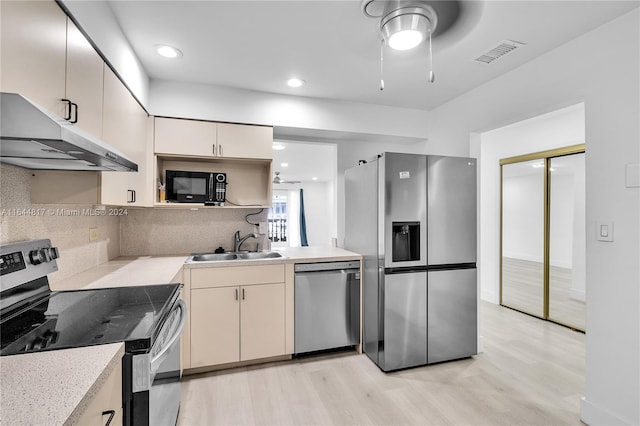 kitchen featuring appliances with stainless steel finishes, cream cabinets, light wood-type flooring, and backsplash