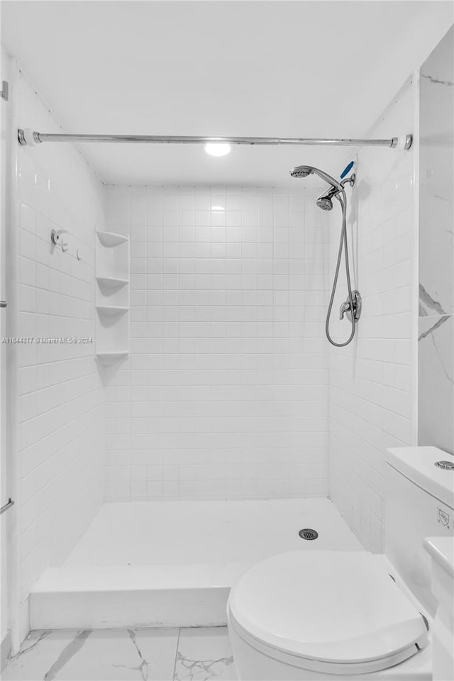 bathroom with tile patterned floors, tiled shower, and toilet