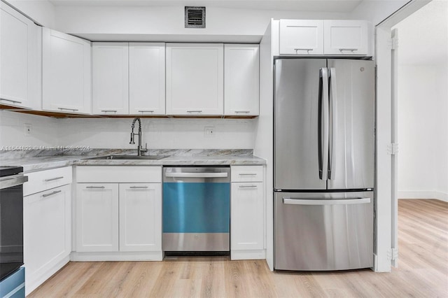 kitchen with light wood-type flooring, tasteful backsplash, white cabinetry, sink, and stainless steel appliances