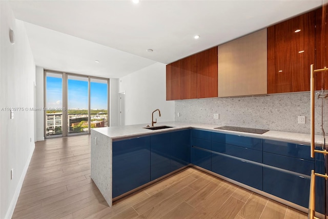 kitchen featuring kitchen peninsula, black electric stovetop, backsplash, sink, and a wall of windows