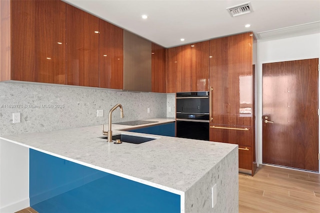 kitchen with sink, tasteful backsplash, light stone counters, light hardwood / wood-style flooring, and kitchen peninsula