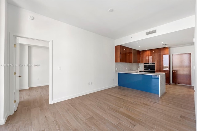 kitchen featuring decorative backsplash, light hardwood / wood-style floors, kitchen peninsula, and black double oven