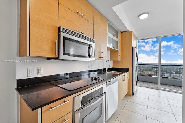 kitchen featuring dark stone counters, stainless steel appliances, light tile patterned floors, and sink