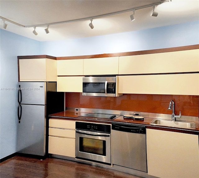 kitchen with appliances with stainless steel finishes, sink, stainless steel counters, dark hardwood / wood-style flooring, and track lighting