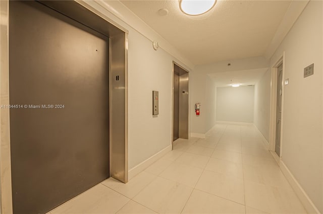 hallway featuring elevator, a textured ceiling, and light tile patterned floors