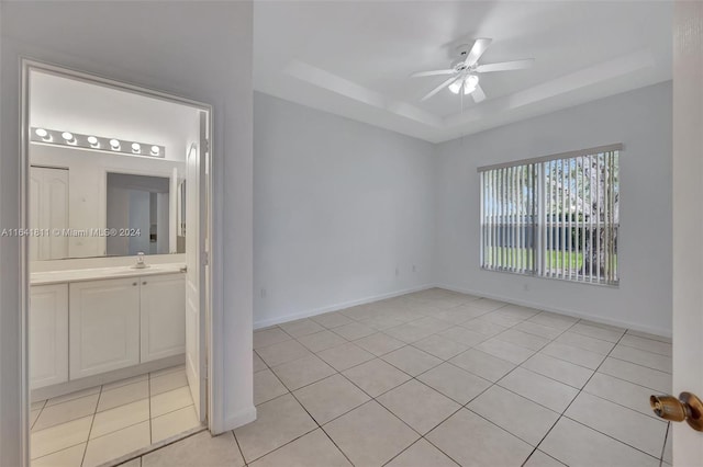 unfurnished bedroom featuring sink, light tile patterned floors, ensuite bath, a tray ceiling, and ceiling fan