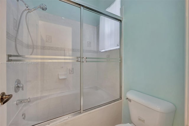 bathroom featuring toilet and bath / shower combo with glass door