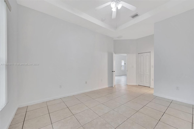 tiled empty room featuring ceiling fan and a raised ceiling