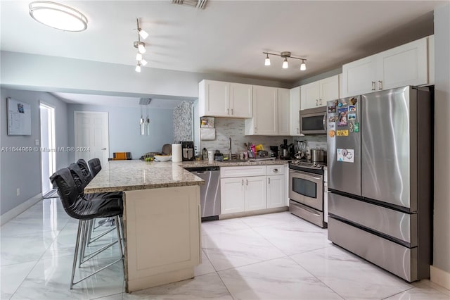 kitchen with track lighting, a kitchen bar, white cabinetry, kitchen peninsula, and stainless steel appliances