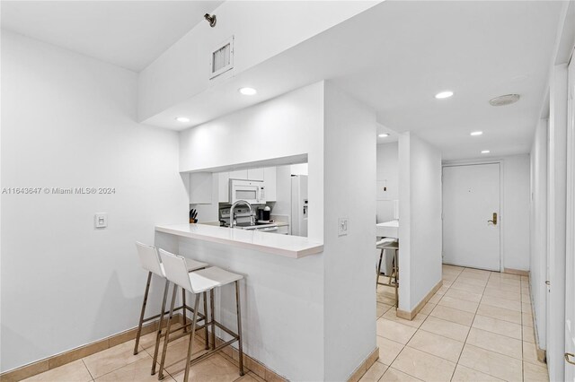 kitchen featuring a kitchen breakfast bar, white cabinetry, light tile patterned floors, and sink