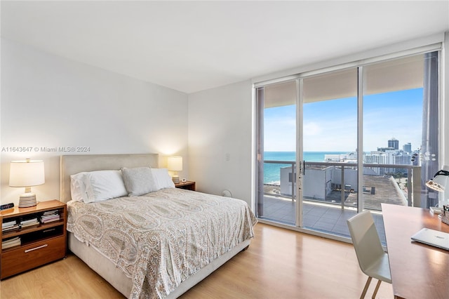 bedroom with light hardwood / wood-style flooring, access to exterior, expansive windows, and a water view