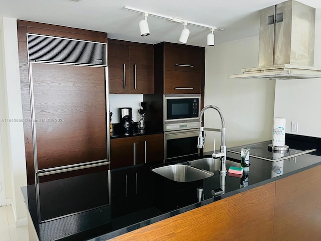 kitchen with wall chimney exhaust hood, dark brown cabinets, sink, black appliances, and track lighting