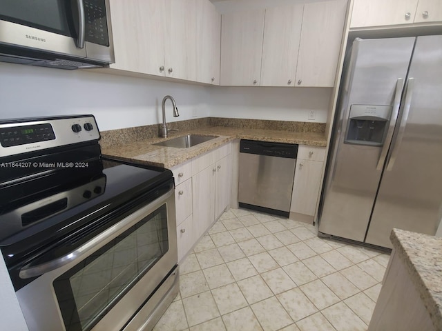 kitchen with light tile patterned floors, appliances with stainless steel finishes, sink, and light stone counters