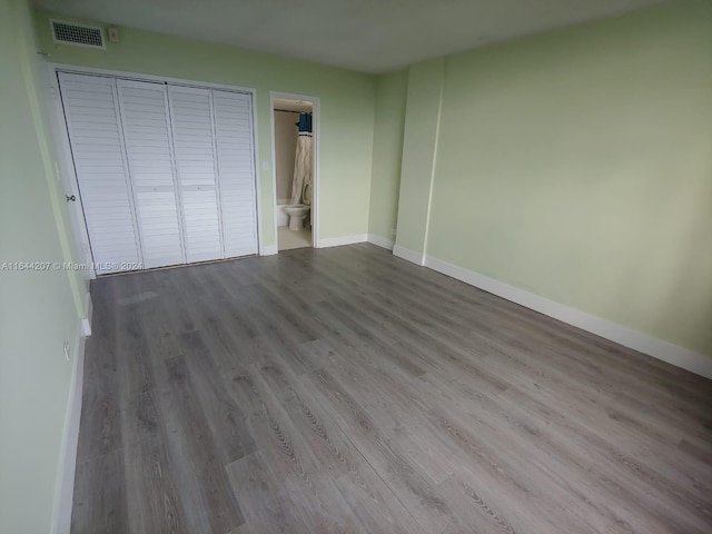 unfurnished bedroom featuring hardwood / wood-style flooring, a closet, and ensuite bath