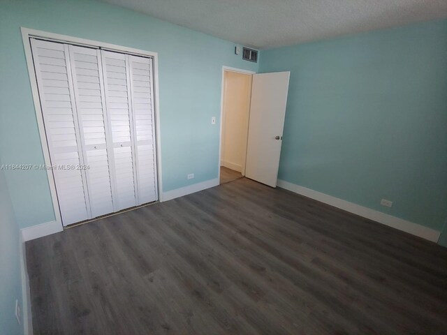 unfurnished bedroom featuring a textured ceiling, a closet, and dark wood-type flooring