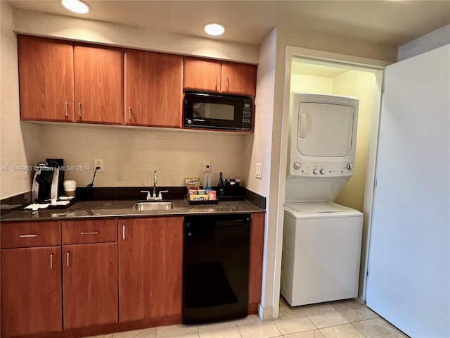 kitchen with sink, stacked washer / dryer, dark stone counters, and black appliances