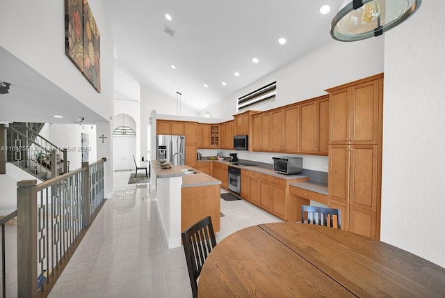 kitchen with sink, appliances with stainless steel finishes, light tile patterned floors, high vaulted ceiling, and a kitchen island with sink