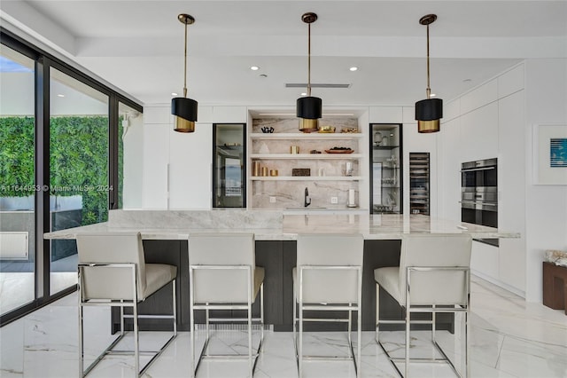 kitchen with white cabinetry, stainless steel double oven, a kitchen breakfast bar, and decorative light fixtures