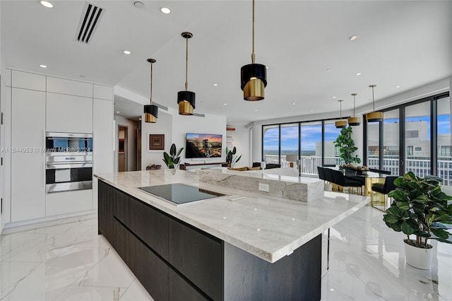 kitchen featuring a spacious island, light stone countertops, cooktop, light tile patterned floors, and white cabinets