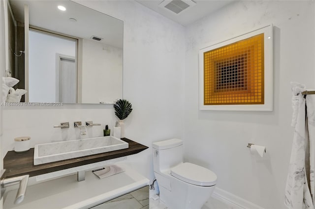 half bath featuring toilet, baseboards, visible vents, and a sink